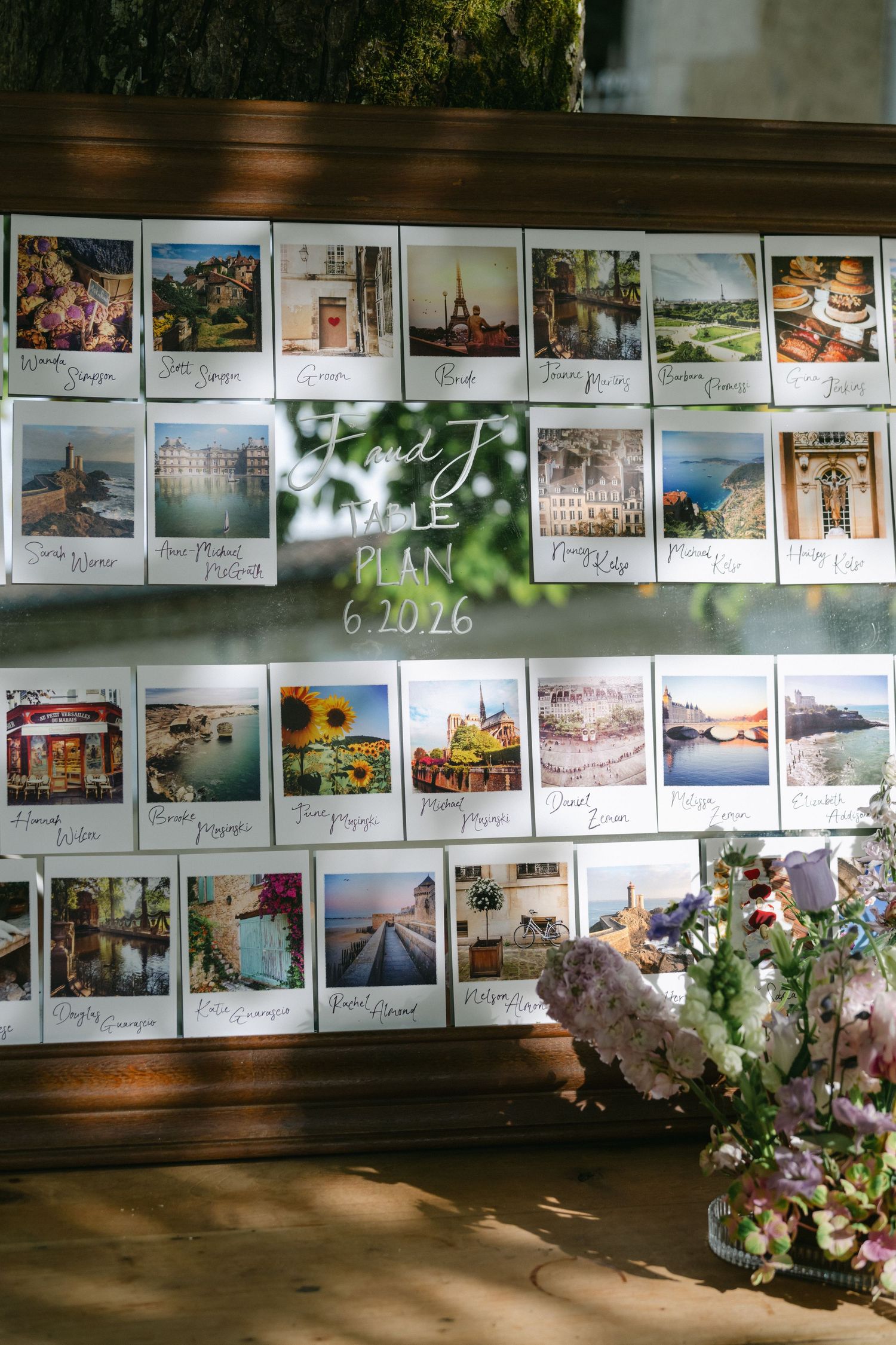 Polaroid photo wedding seating chart display on wooden board with travel photos and floral arrangements dated 6.20.26.