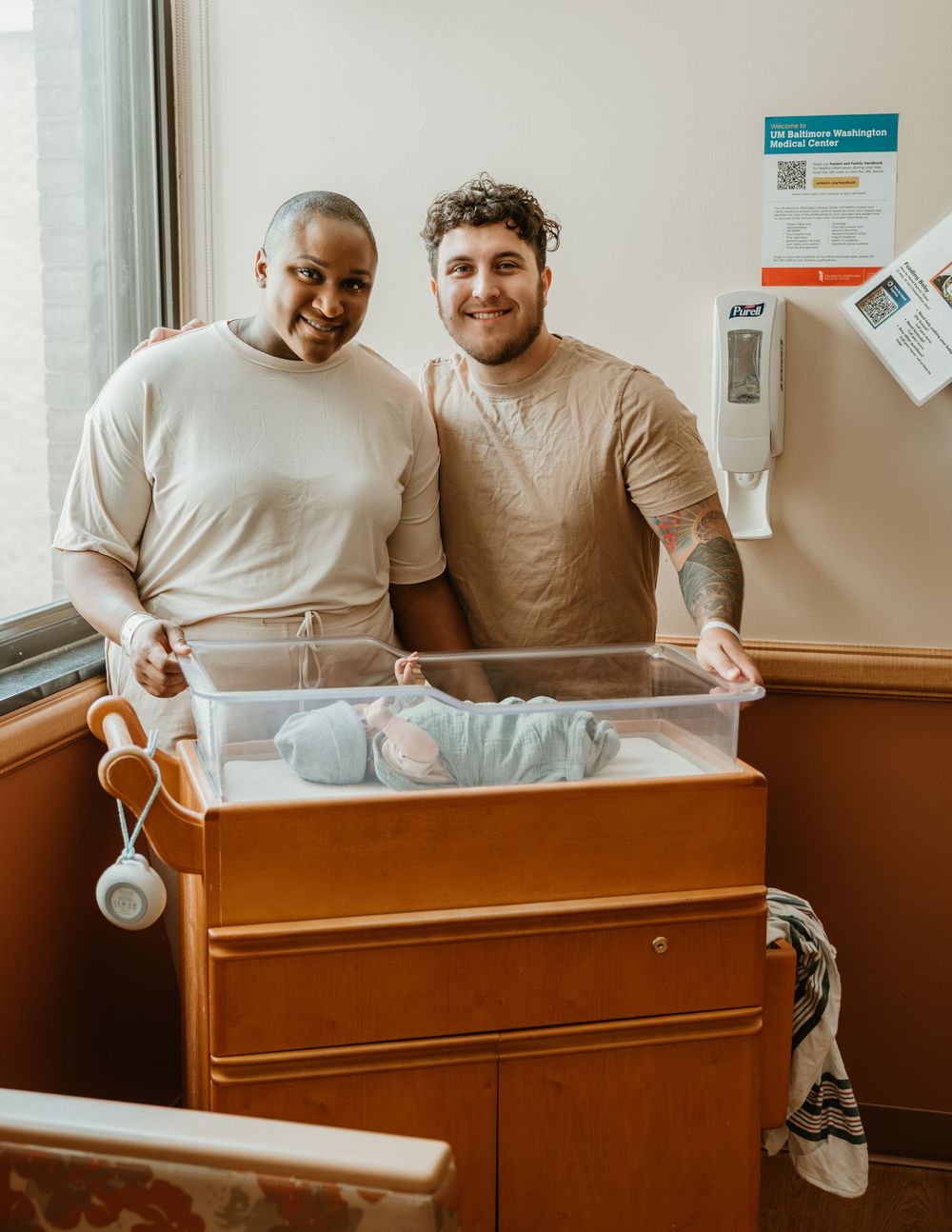Two proud parents smile beside their newborn baby in a hospital bassinet, celebrating the arrival of their child.