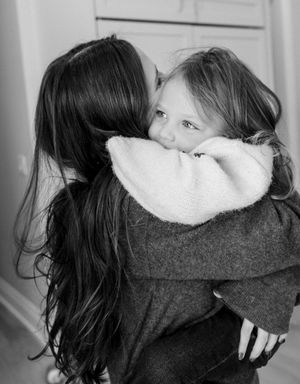 Black and white photo of a woman hugging a young girl in a sherpa jacket, the child looking over her shoulder.