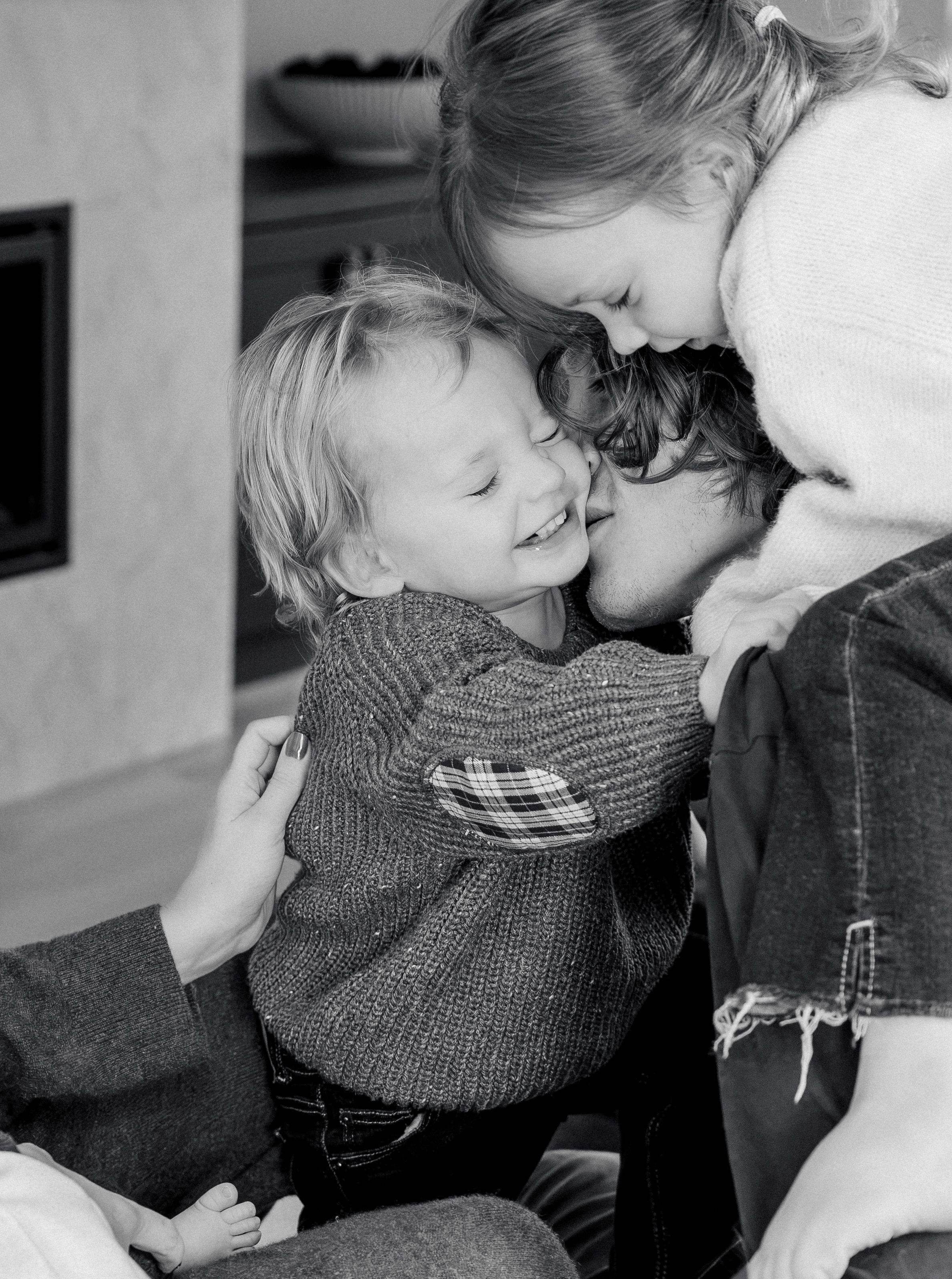 Black and white photo of two young children joyfully hugging an adult in a cozy living room setting.