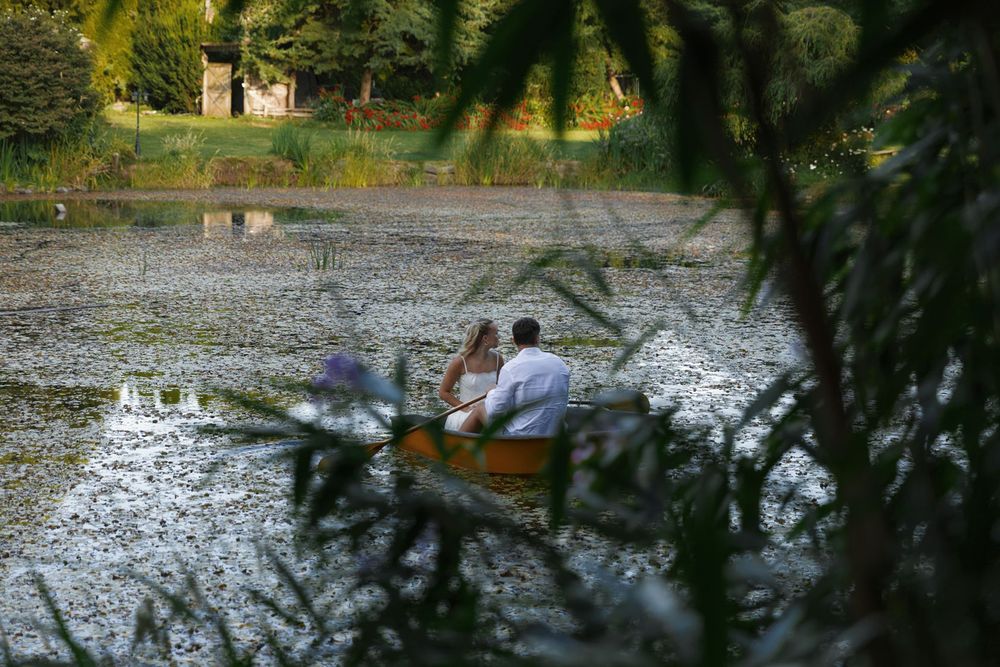 Romantic couple rowing a wooden boat on a serene lake, framed by lush green foliage.