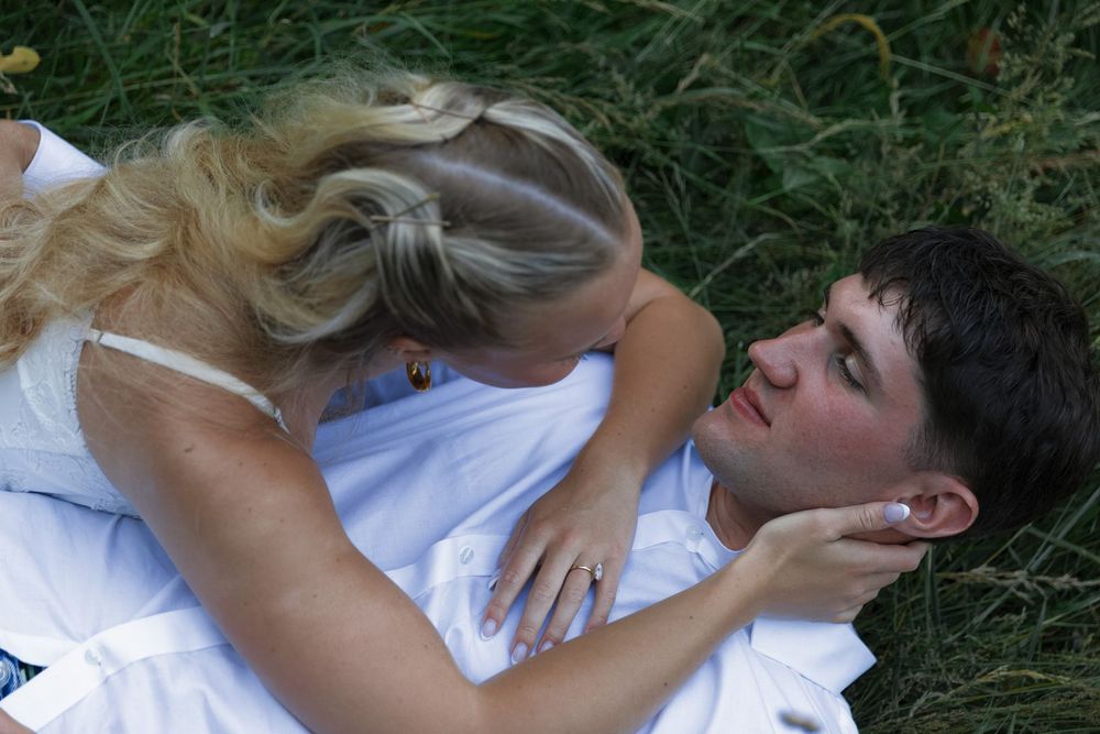 A young couple lying in green grass, sharing a romantic moment as the blonde woman leans in close to the man.