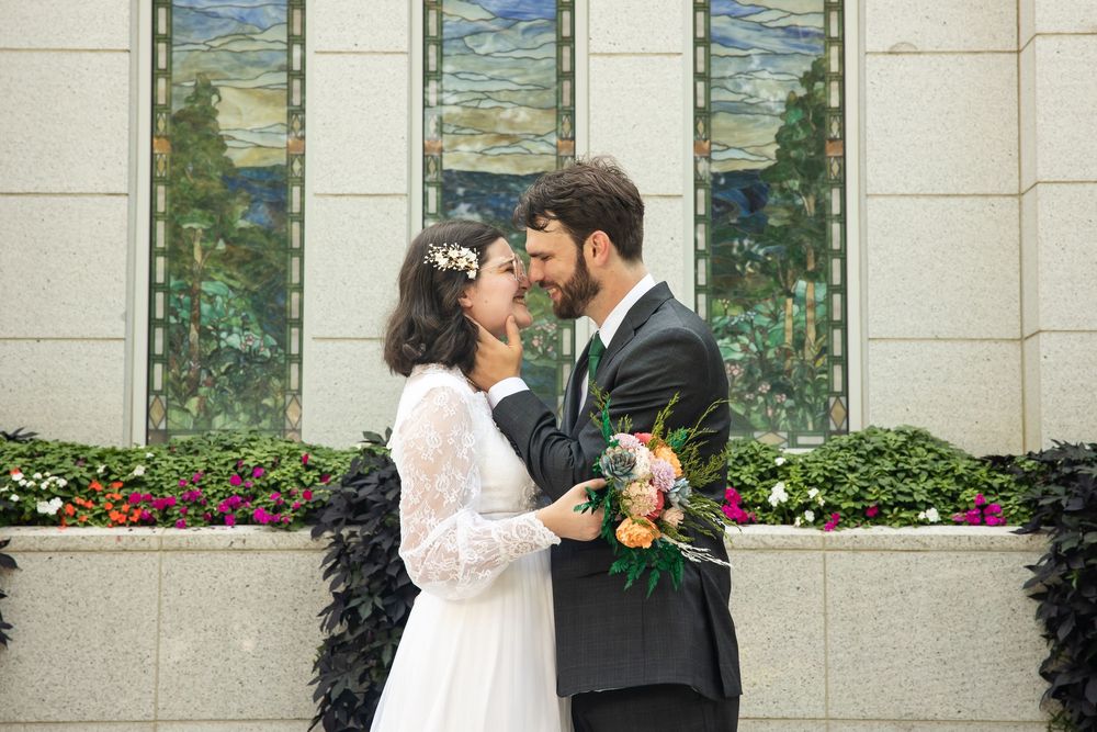 Bride and groom sharing a romantic moment outside a decorated wedding venue with colorful flowers and stained glass windows.