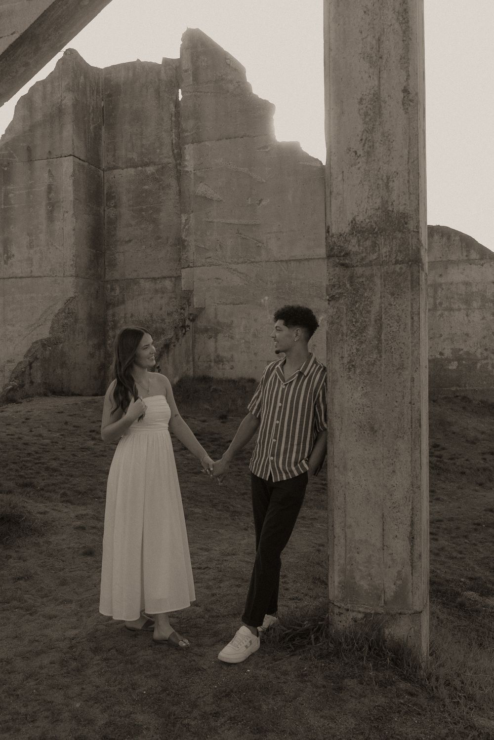 Black and white photo of couple holding hands near concrete columns at historic ruins.