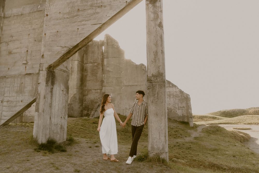 Couple holding hands near rustic concrete ruins outdoors during golden hour engagement photo session.