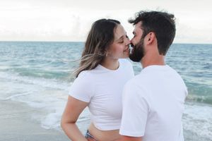 Couple sharing a romantic moment nearly kissing on a beach with ocean backdrop.