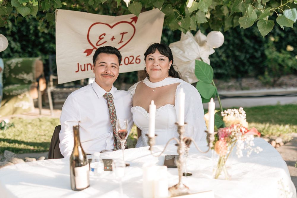Bride and groom sit at sweetheart table cuddling at backyard wedding reception in Los Angeles.