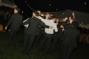 Group of men in black suits dancing outdoors at night during a festive celebration or wedding reception.