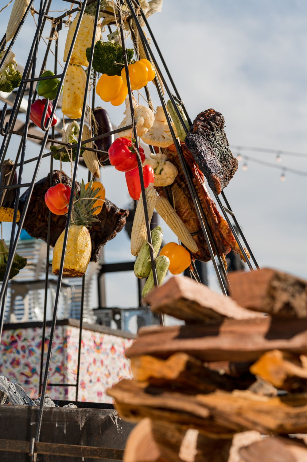 Colorful dried fruits and vegetables hanging on a metal frame outdoors with stacked wood in the foreground.