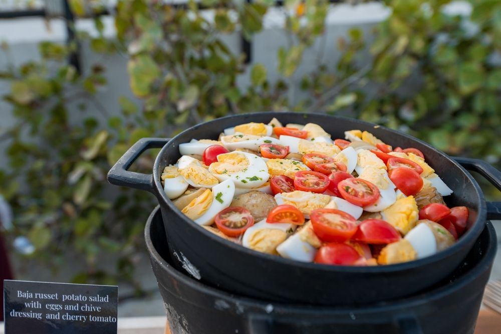 Russet potato salad with eggs, cherry tomatoes, and chive dressing served in a cast iron skillet outdoors.