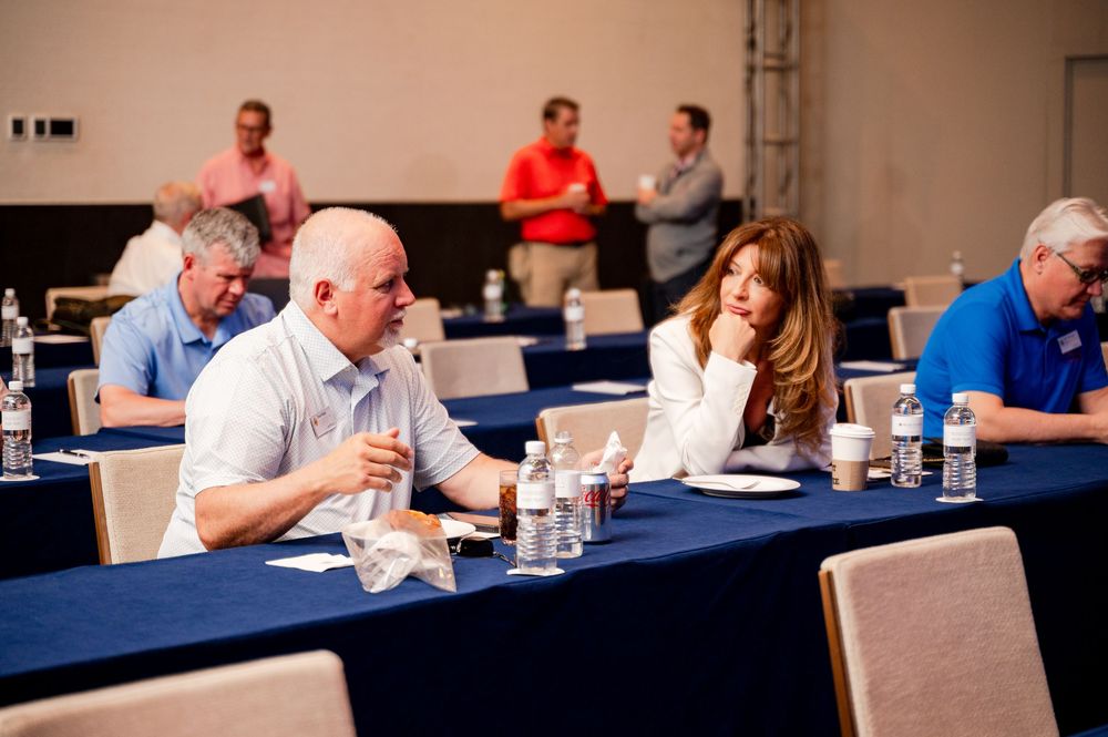 Professionals networking at a conference table during a business meeting in a modern event hall.
