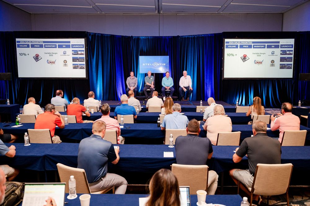 Conference panel discussion with four speakers on stage presenting to an audience in a corporate event setting.