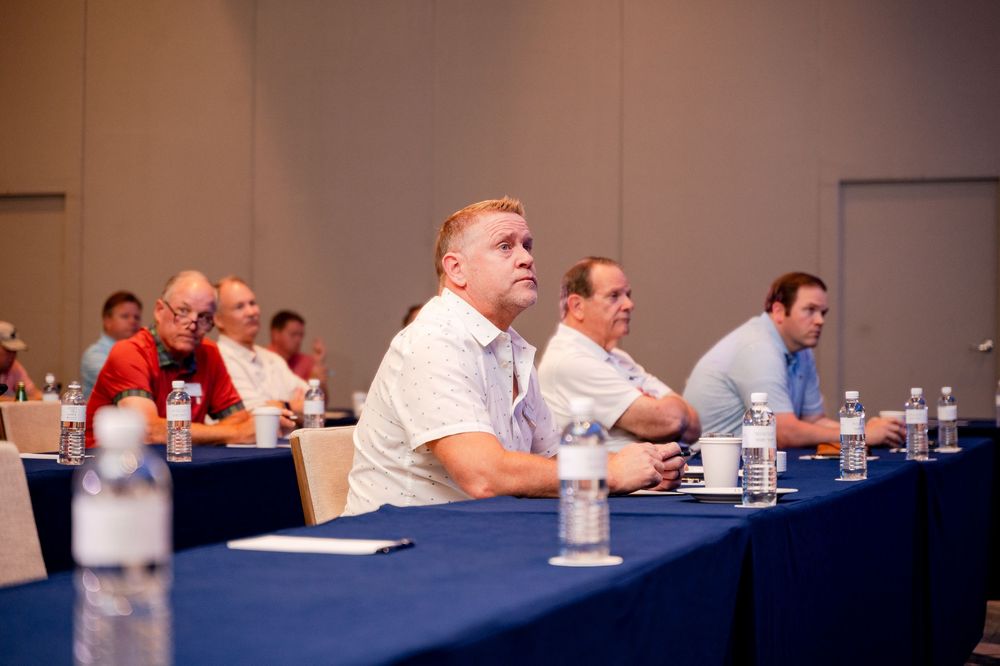 Business professionals seated at conference tables during a corporate meeting or seminar in a modern venue.