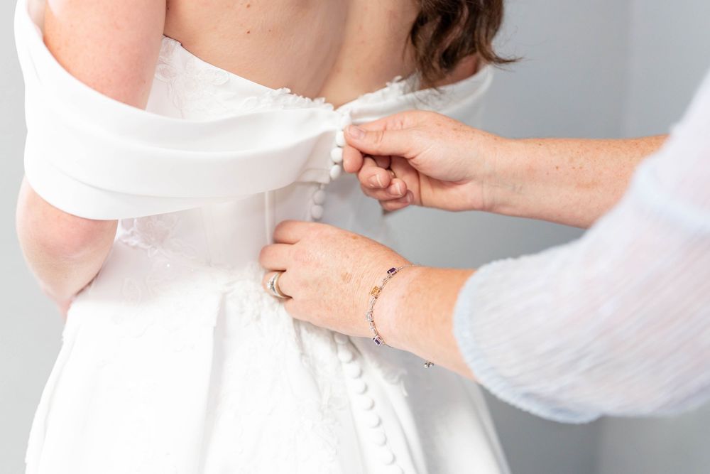 mom fastens the back of a white wedding dress on a bride during bridal preparations.