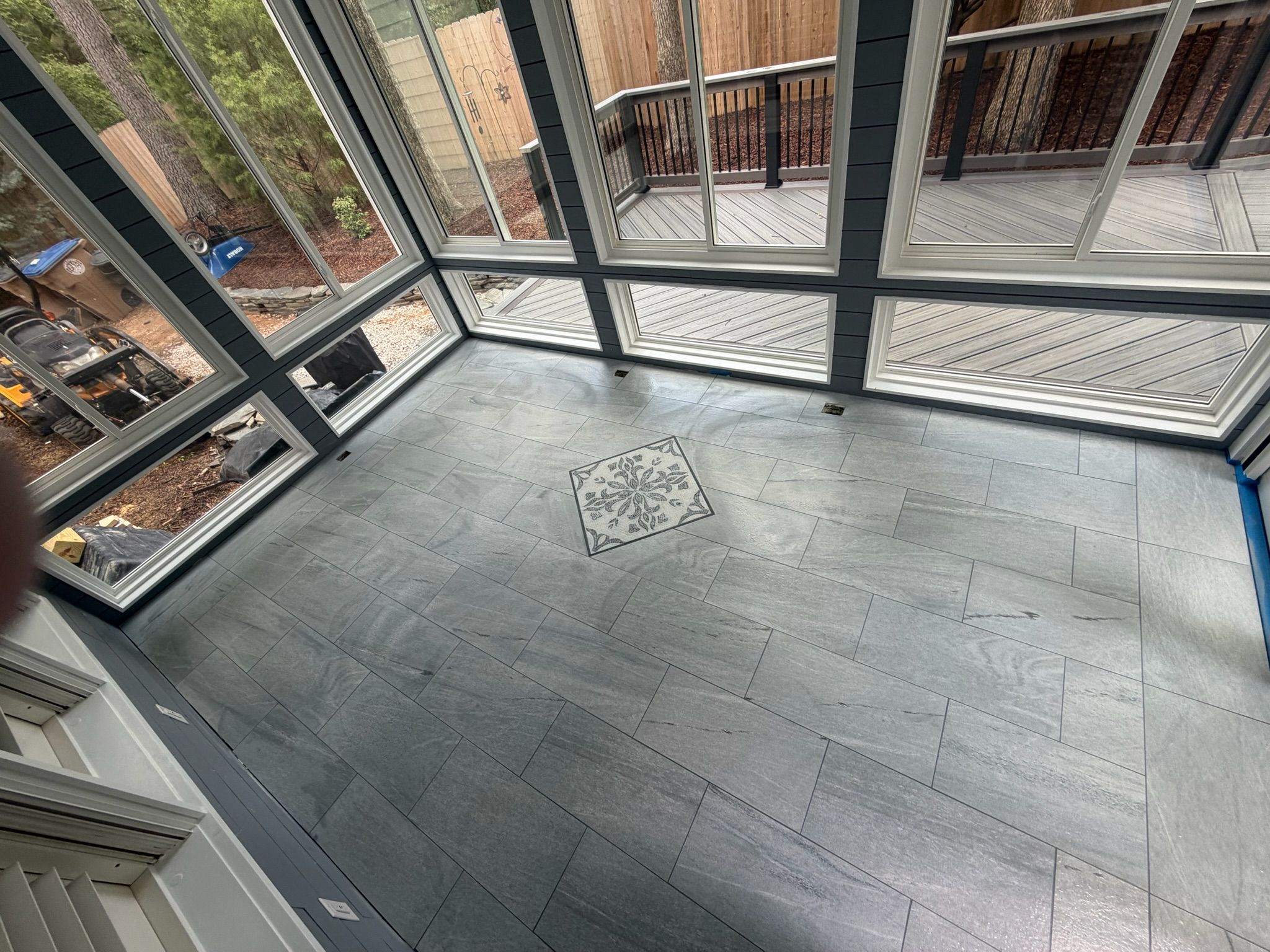 Overhead view of gray slate tile floor with ornate mosaic medallion centerpiece in a glass-enclosed sunroom.