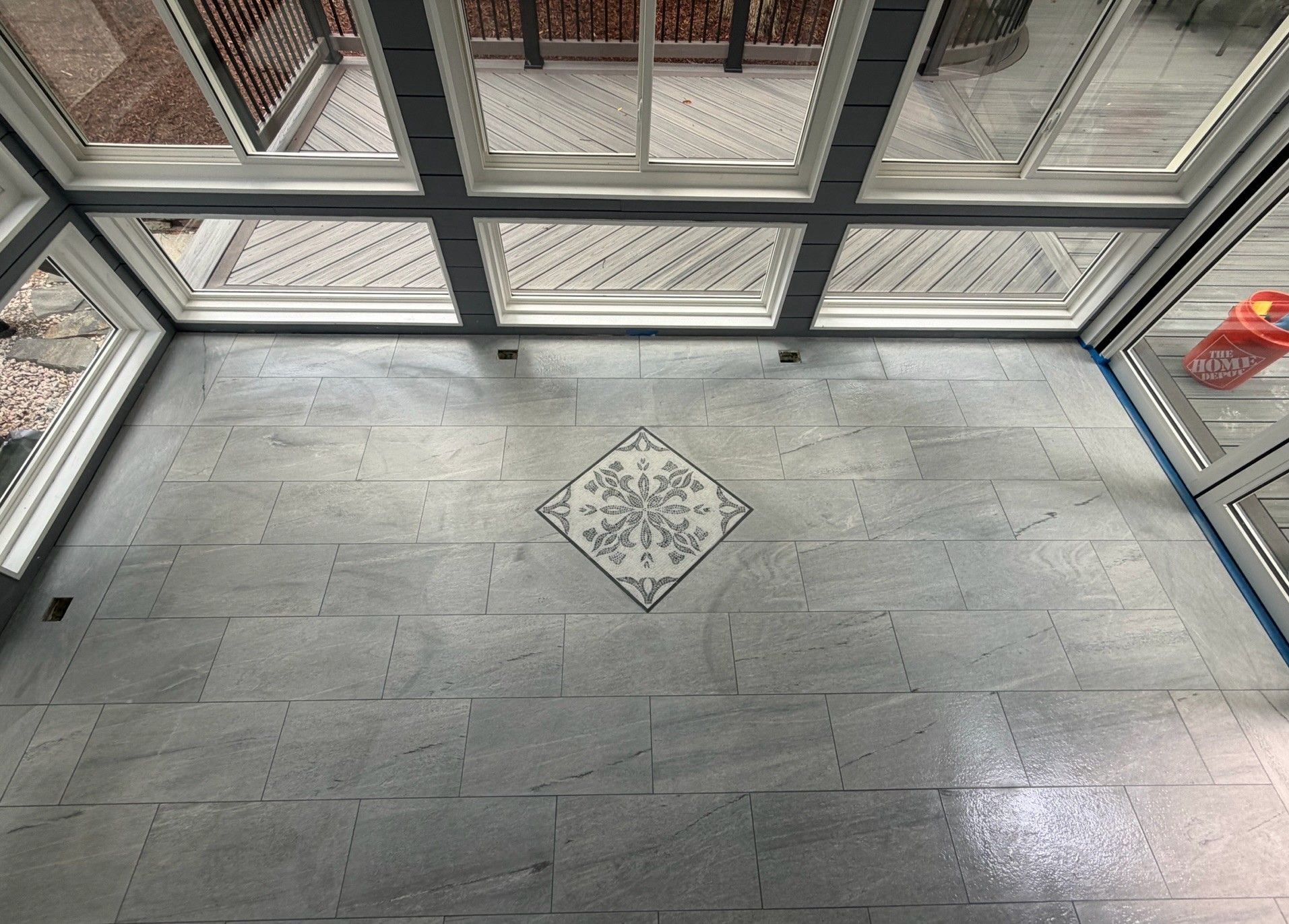 Close-up of gray porcelain tile floor featuring an elegant decorative mosaic inlay medallion in a sunroom.