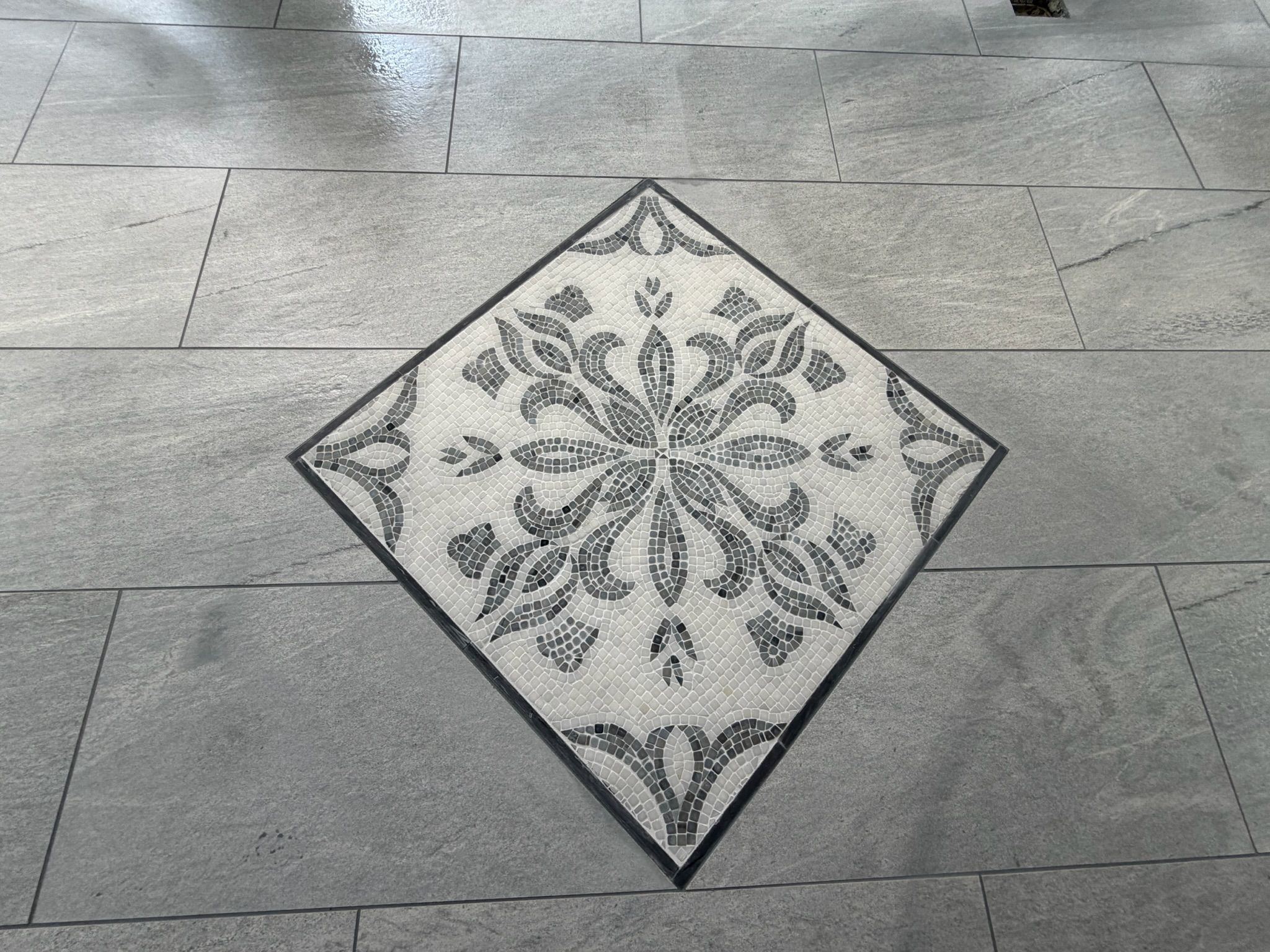 Detailed view of an intricate floral mosaic tile medallion set in diamond orientation on gray tile floor.