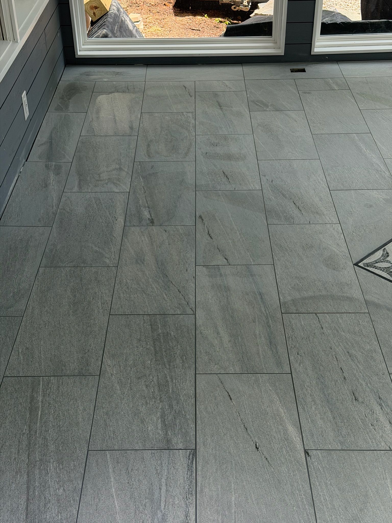 Large format gray slate porcelain tiles with natural stone veining installed on an outdoor sunroom floor.