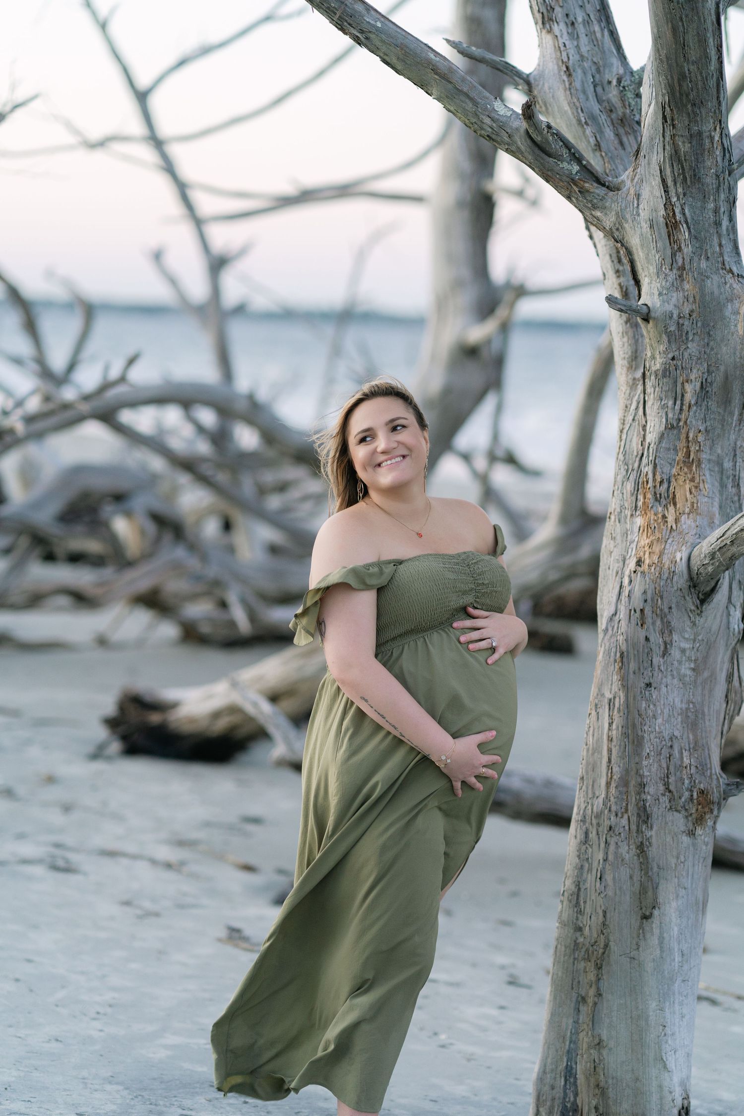 Expectant mother in a flowing green dress beside the driftwood trees at Jekyll Island.