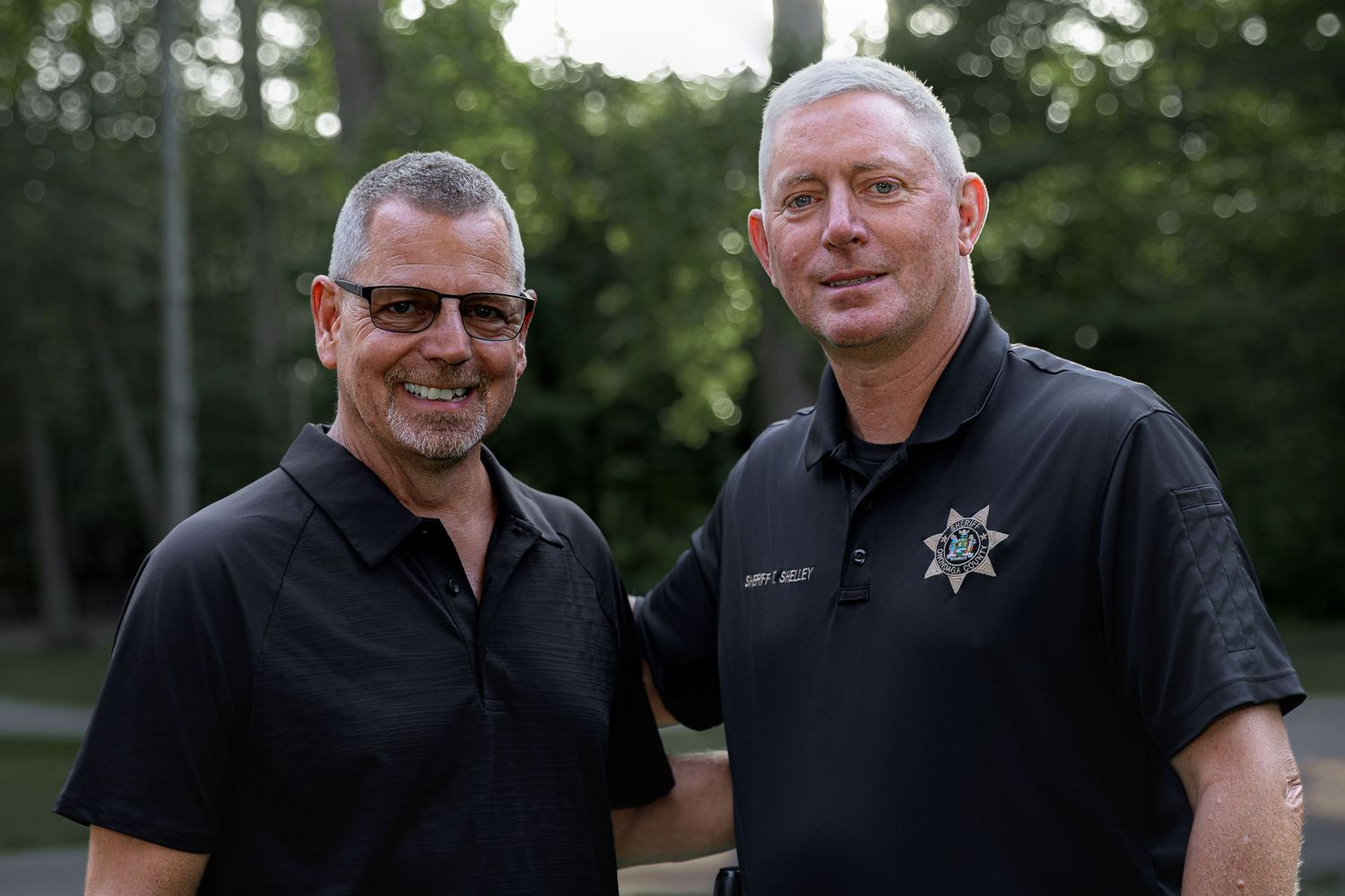 Two men in black polo shirts smiling outdoors at a casual evening event.