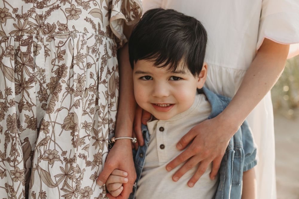 A young smiling boy in a white polo shirt hugs his mother outdoors in a warm family portrait.