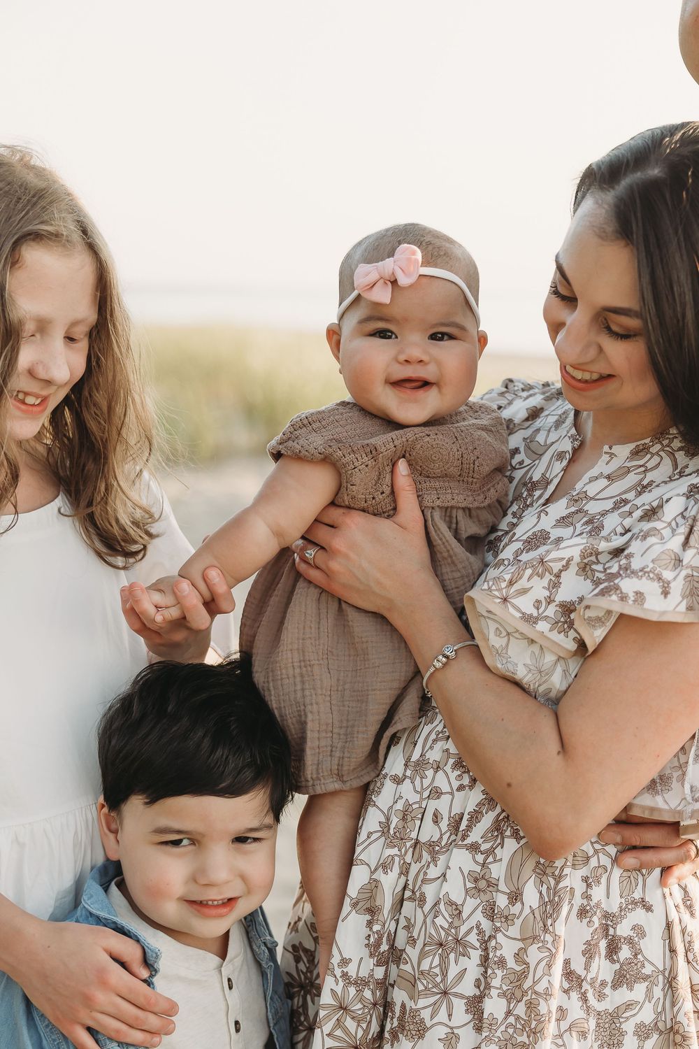 A mother holds a smiling baby while two children gather close for a warm family portrait outdoors.
