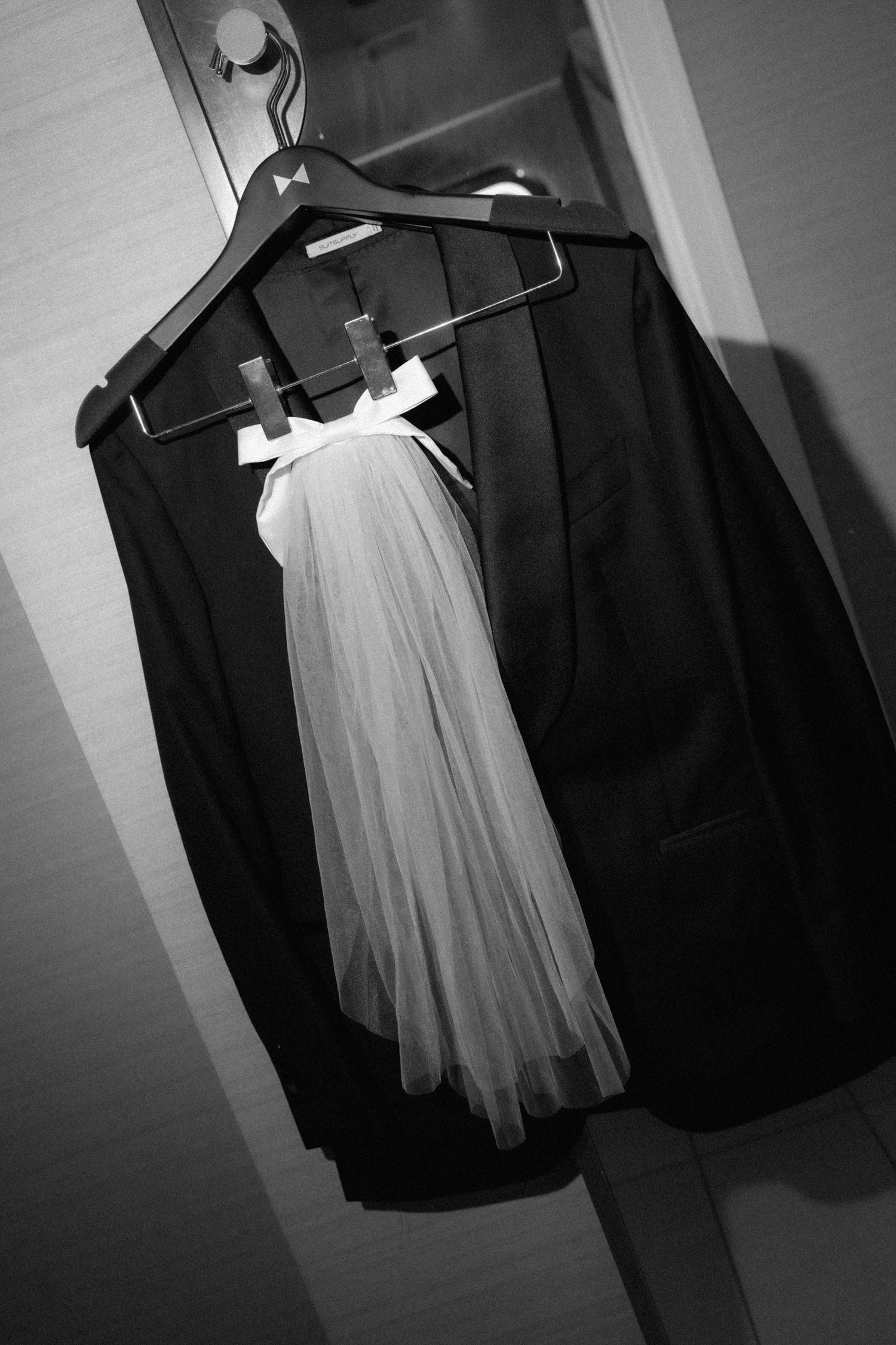A bride in a white mini dress and groom in a black tuxedo share a romantic moment in an elegant hotel room.
