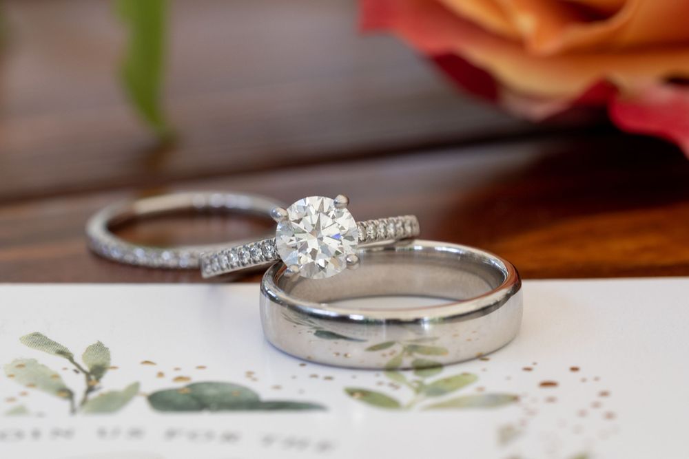 Three wedding rings, including a diamond solitaire engagement ring and two bands, displayed on a card with a flower.