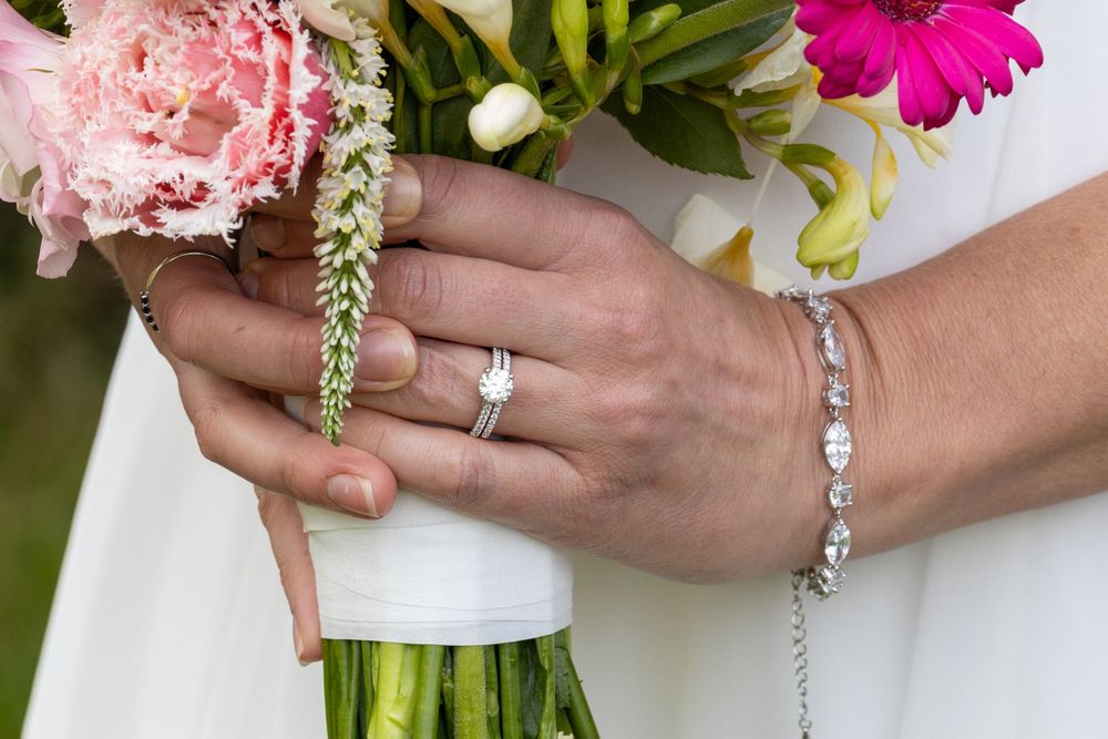 Close-up of bride's hands holding floral bouquet, wearing diamond engagement ring and elegant tennis bracelet.