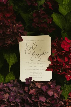 Elegant wedding invitation for Kyla and Brayden surrounded by lush purple and red hydrangea flowers.