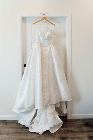 Elegant white ball gown wedding dress with floral lace detail hanging on wooden hanger over white door.