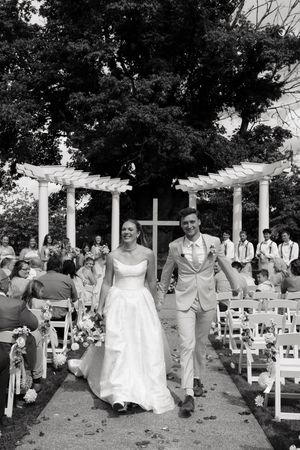 Black and white photo of a joyful bride and groom walking down the aisle after their outdoor wedding ceremony.