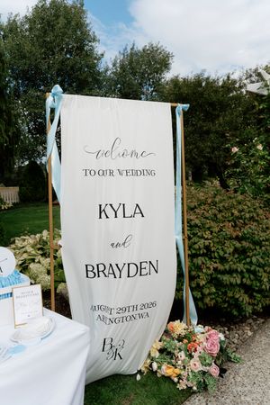Elegant outdoor wedding welcome sign for Kyla and Brayden, August 29th 2026, Arlington WA, adorned with blue ribbons.
