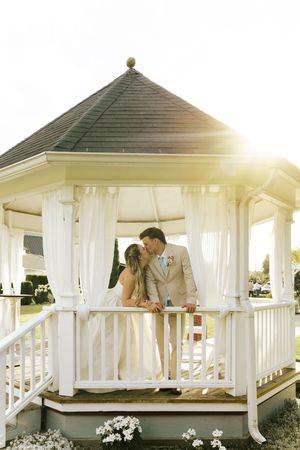 Bride and groom sharing a romantic kiss inside a white gazebo bathed in golden sunlight.