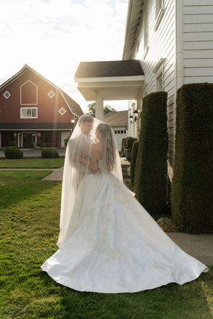 Bride and groom share a romantic kiss under a flowing veil outside a white venue with a red barn backdrop.