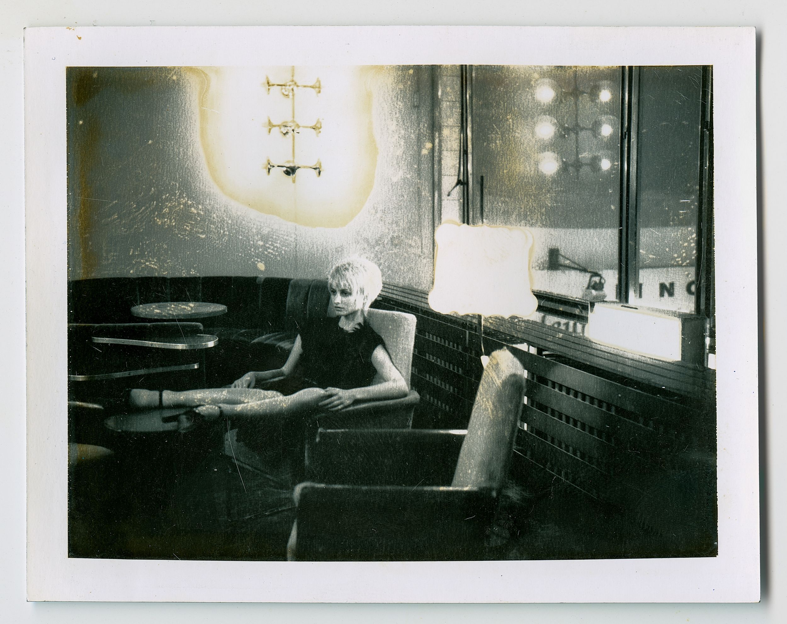 Vintage black and white photo of a person sitting in an armchair inside a dimly lit lounge or bar.