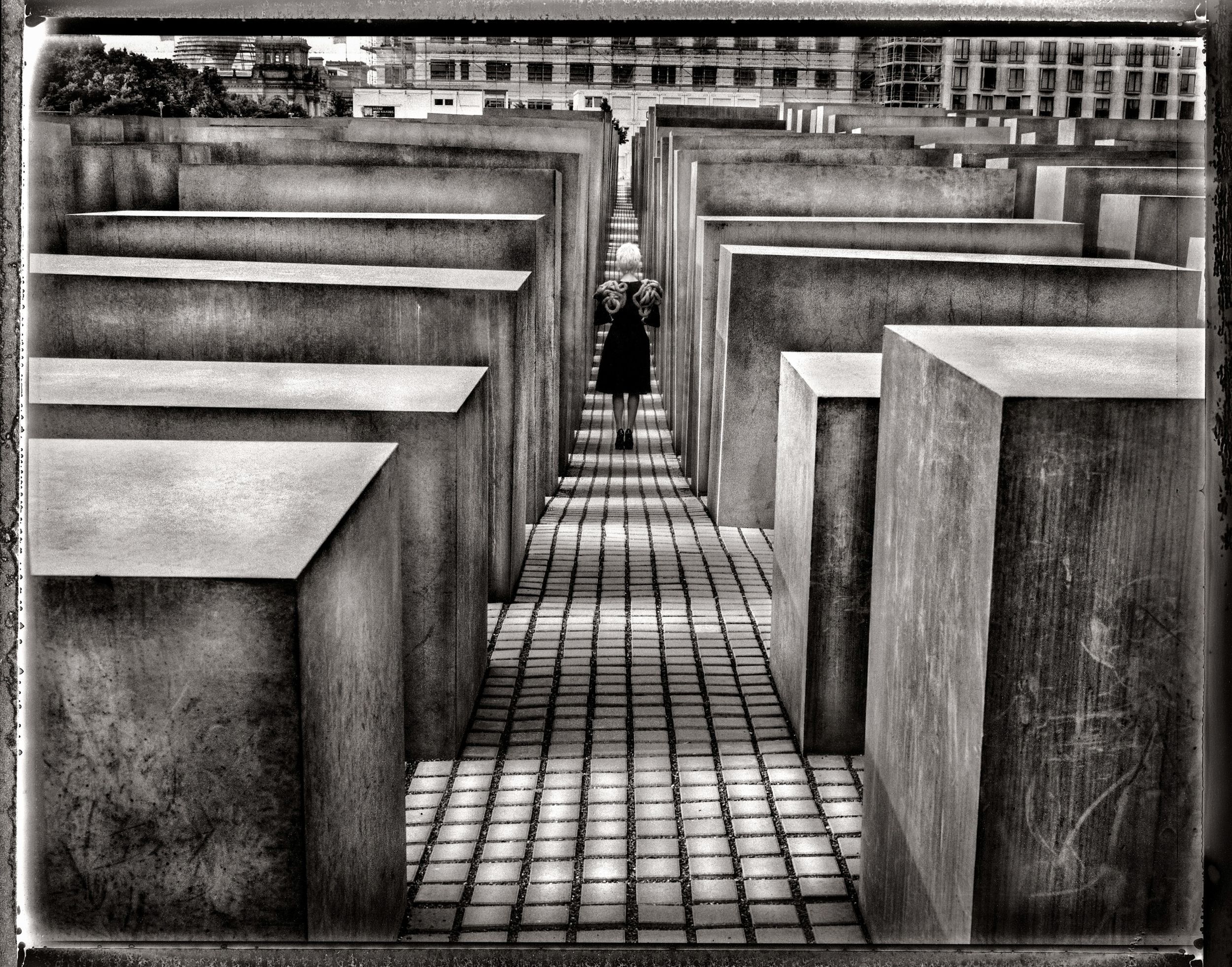 Black and white photo of a person standing among the concrete stelae of the Holocaust Memorial in Berlin, Germany.