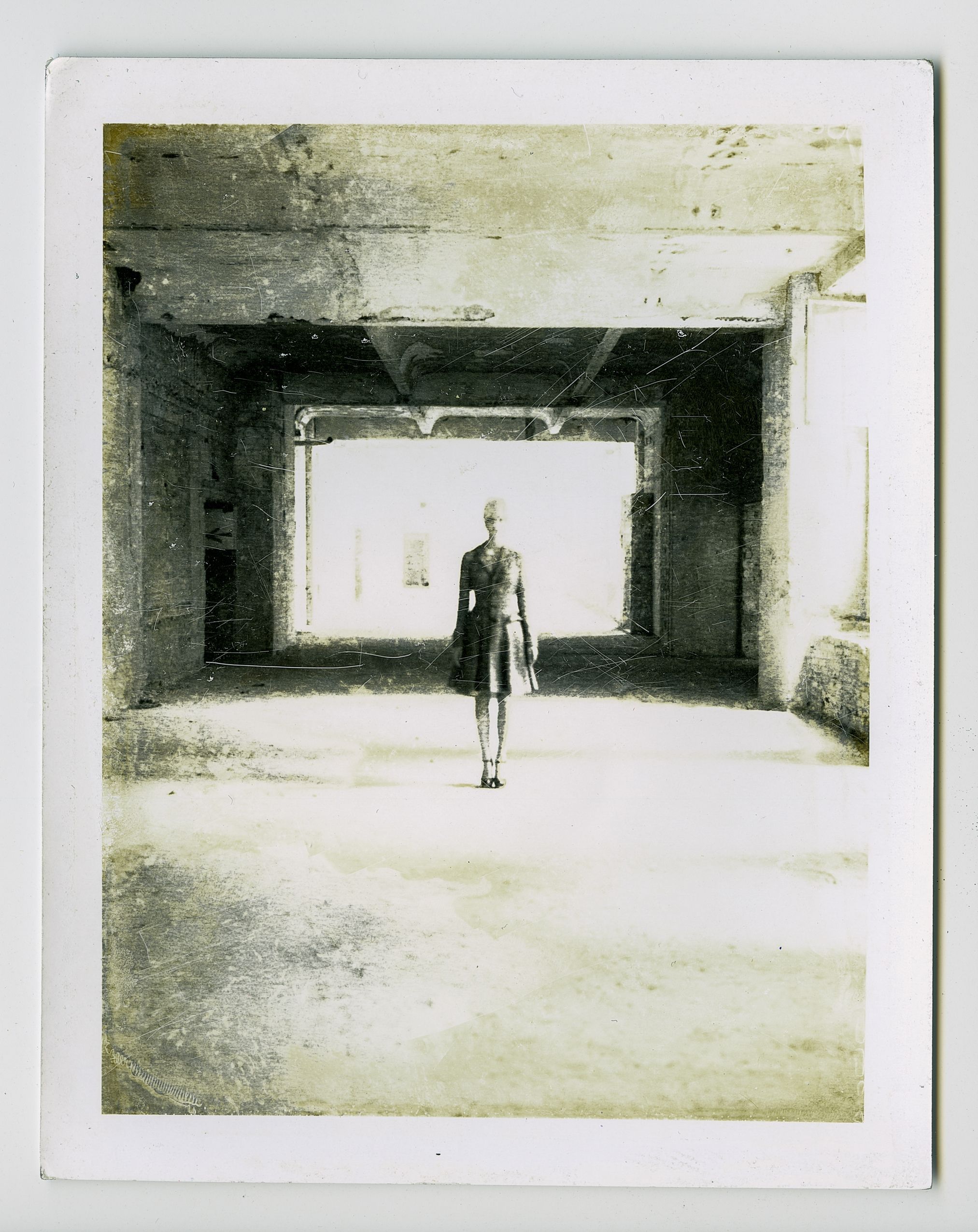 Vintage black and white photo of a lone figure standing in an abandoned industrial building with bright light.