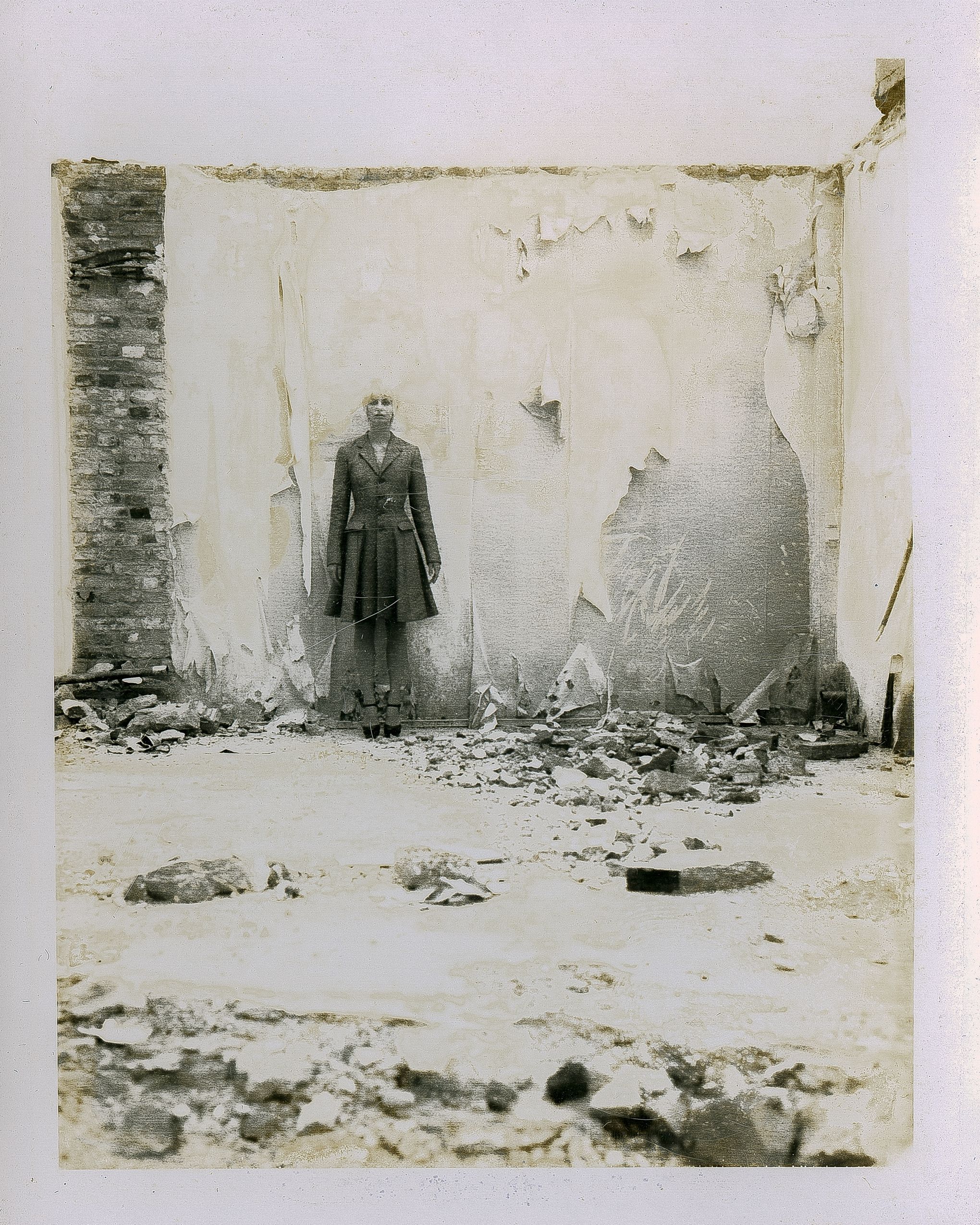 Person standing amid rubble in a destroyed building with crumbling walls and debris scattered across the ground.