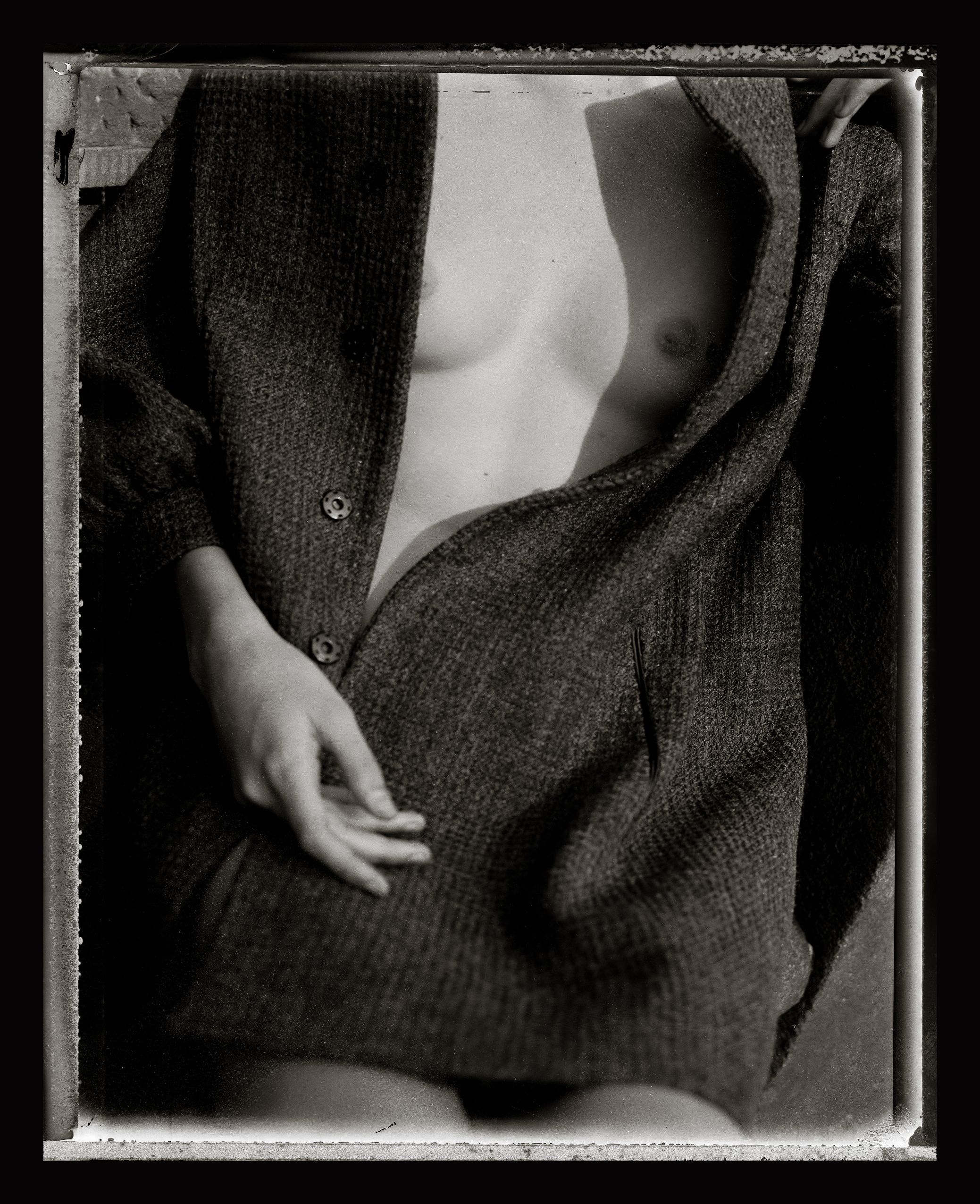 Black and white fine art photograph of a partially open knit cardigan, artistic nude torso study.