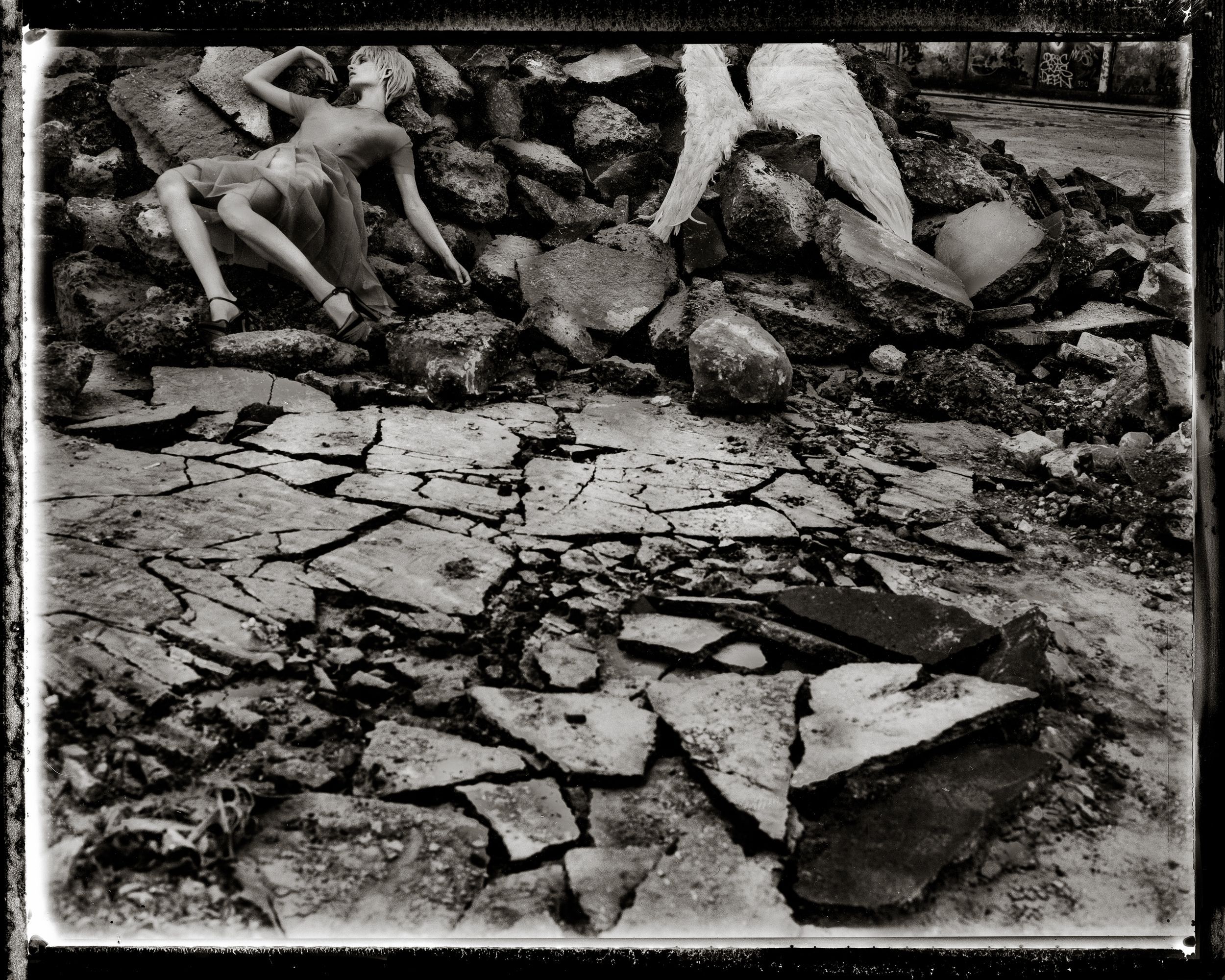 Black and white photo of cracked dry earth with rocky rubble and human figures in the background.