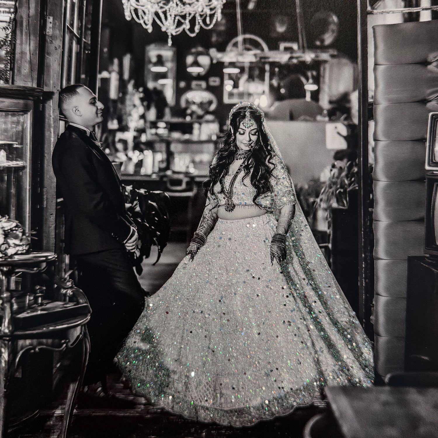 Black and white photo of a bride in a sparkling lehenga and groom in a suit posing in an elegant venue.