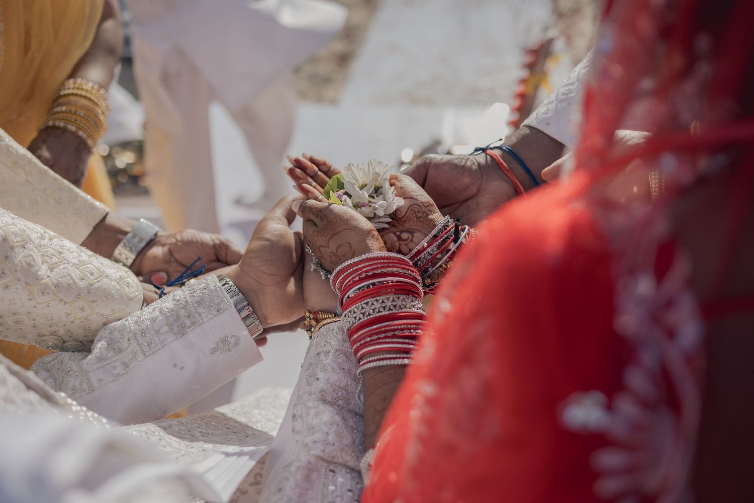 Close-up of Indian wedding ceremony hands exchanging flowers, bride wearing red bangles and traditional bridal attire.