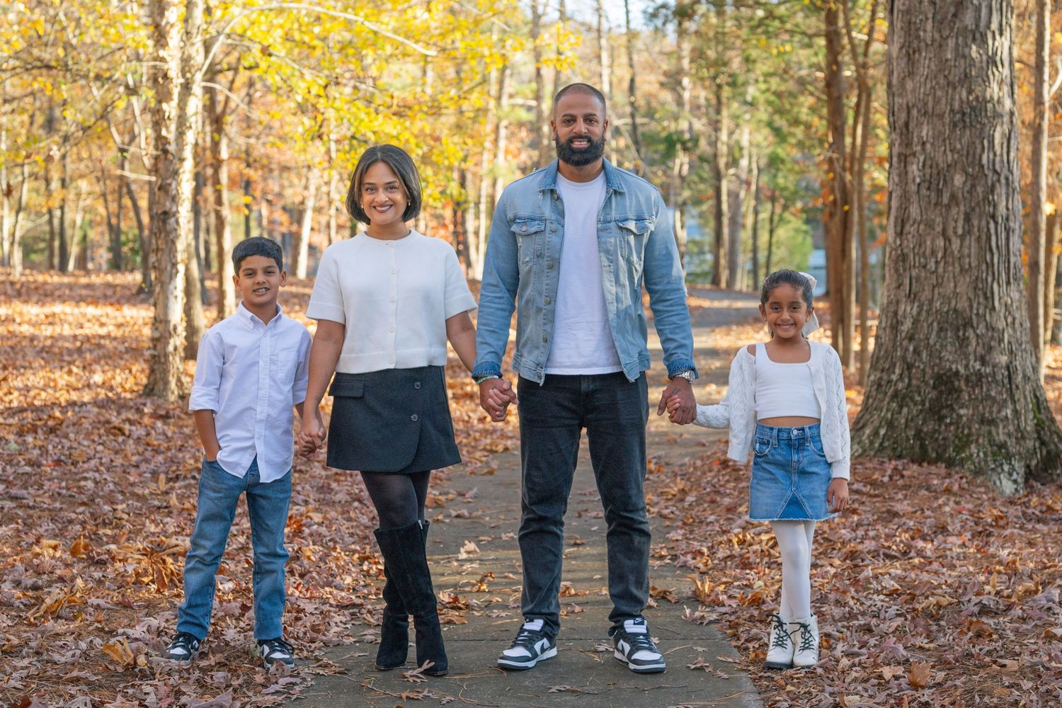 Family of four posing on a forest path surrounded by autumn foliage and fallen leaves.