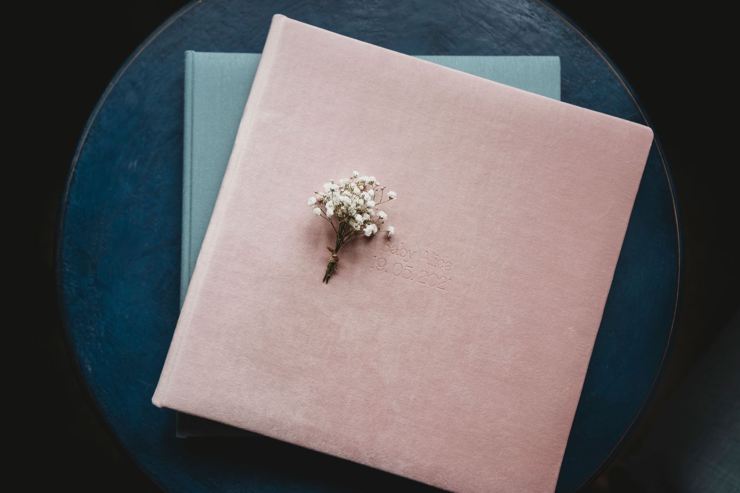 Pink photo album with small white flower arrangement on blue surface.