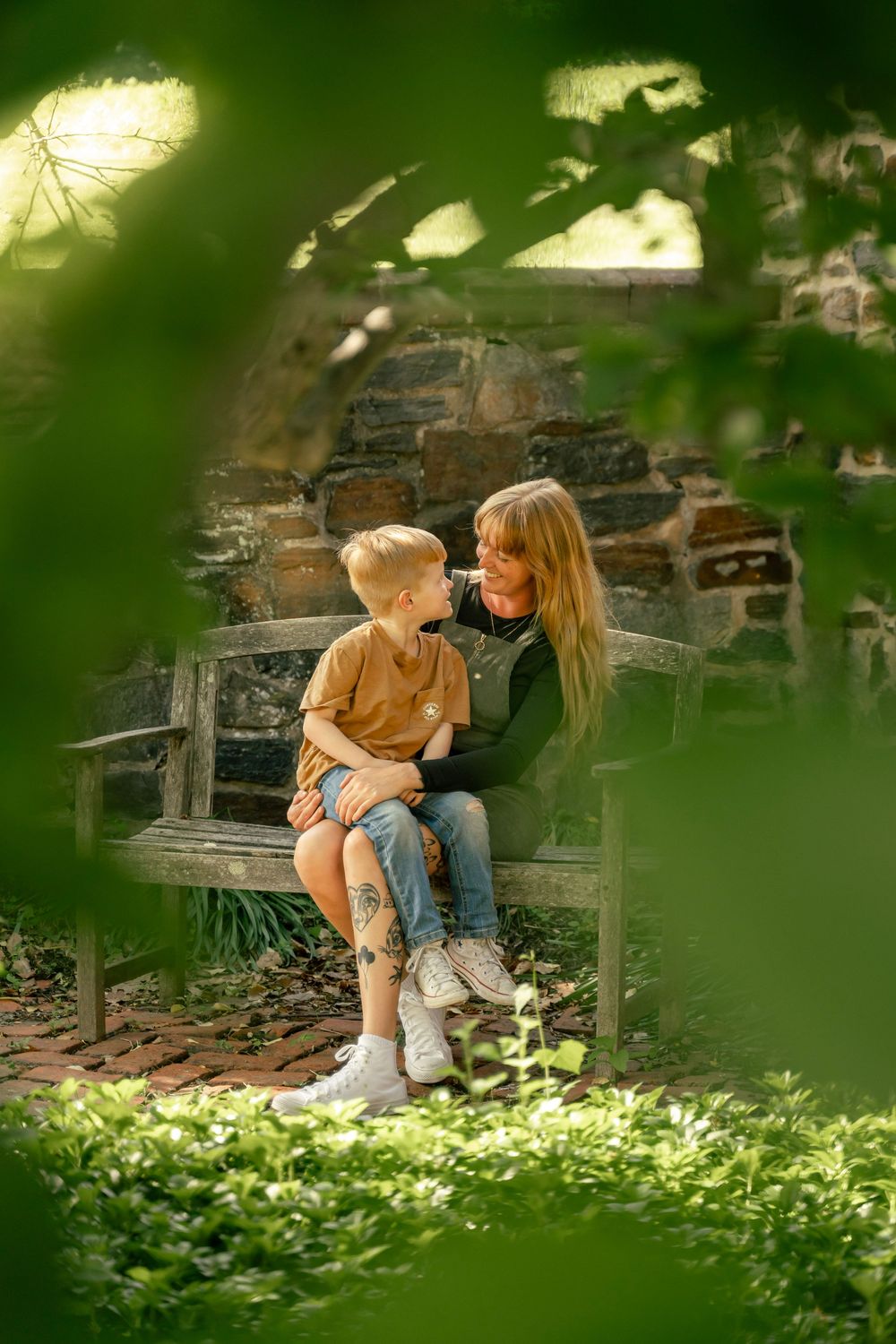 Mother and son sitting on a bench together with foliage in the foreground