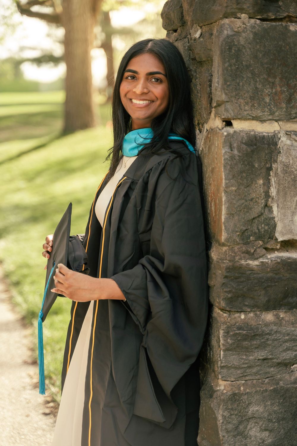 College senior wearing her regalia leaning against a stone pilar