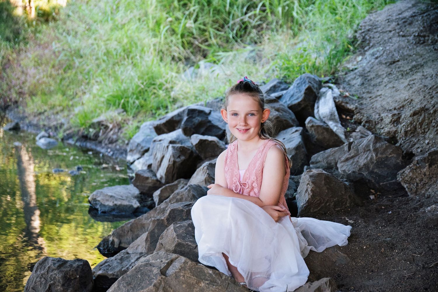 9 year old girl smiling it the camera sitting on the rock on the side of a river in the Gold Coast Hinterland