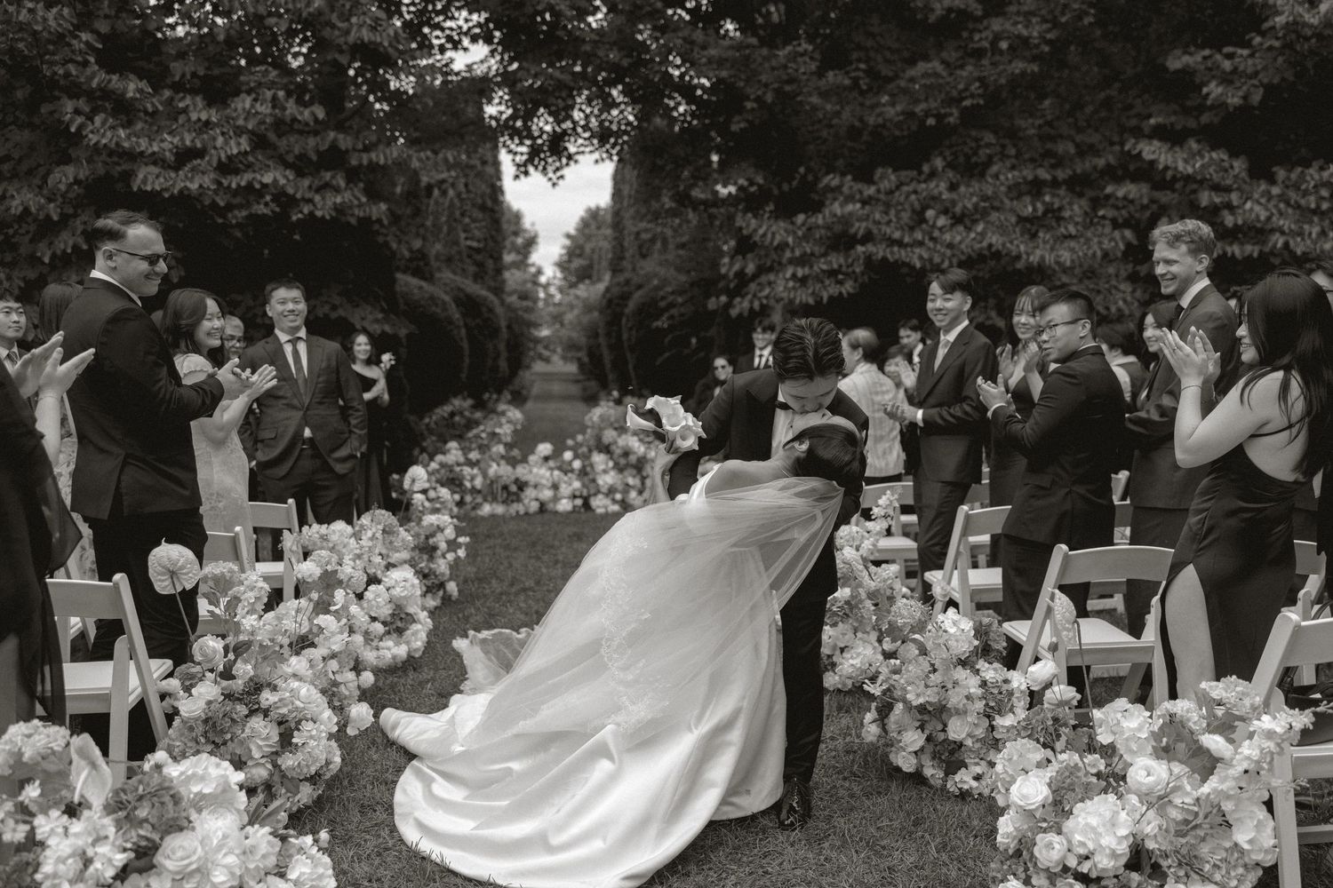 Black and white photo of bride and groom sharing a dip kiss on the aisle at their garden wedding.