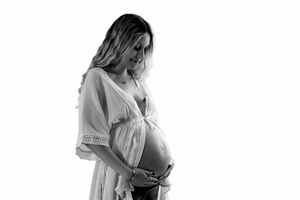 Black and white photo of a pregnant woman in a white dress cradling her baby bump against a white background.